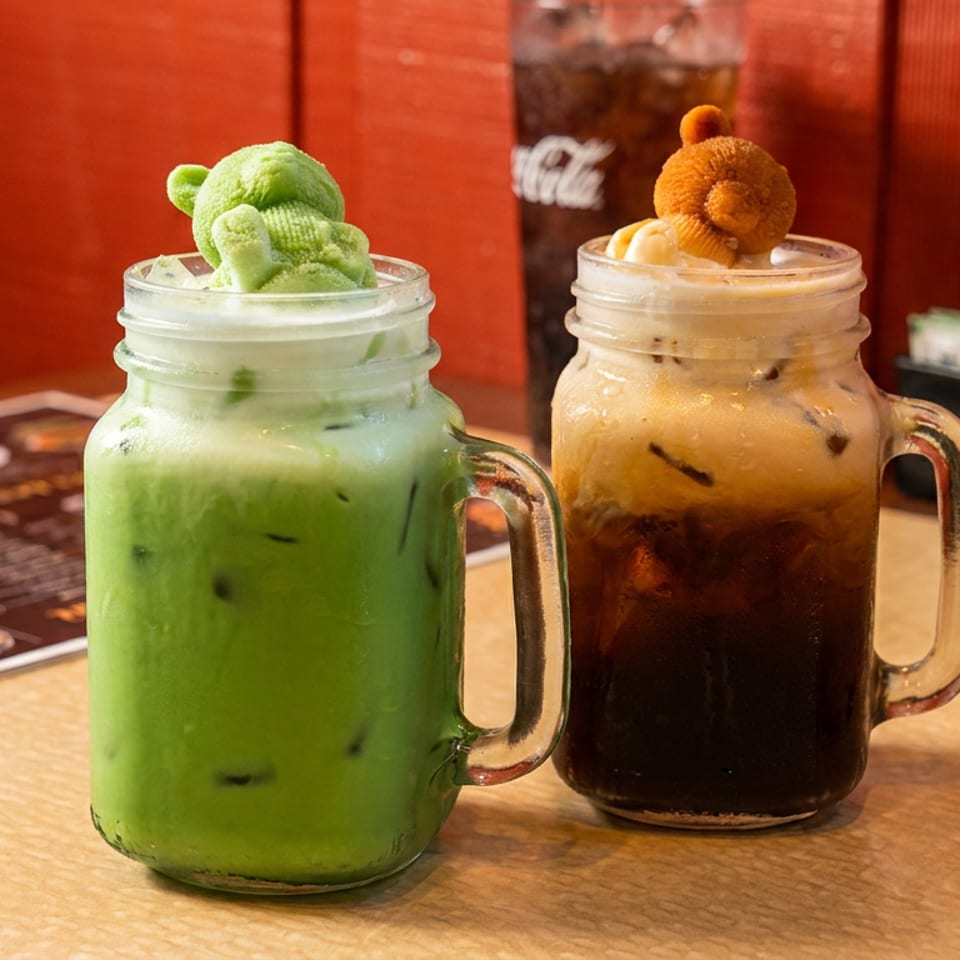 Green and brown iced drinks in glass mugs topped with teddy bear-shaped treats on a restaurant table.