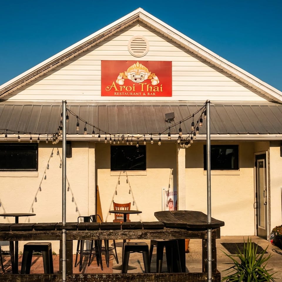 Exterior of Aroi Thai Restaurant & Bar with outdoor seating, string lights, and an open entrance.